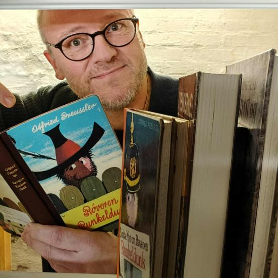 Biblioteksformidler Hans Wendelboe Bøcher med børnebogen "Røveren Runkeldunk", set gennem magasinets bogreoler.