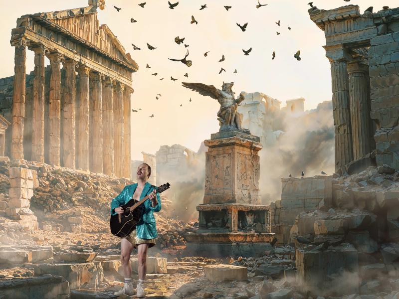 Mand i turkis jakke spiller guitar midt i græske ruiner