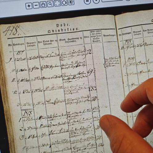 Digitalt opslag i kirkebogen for Brønderslev Sogn, 'døde Qvindekøn 1817'. I forgrunden et par fingre, der læser på skærmen.  